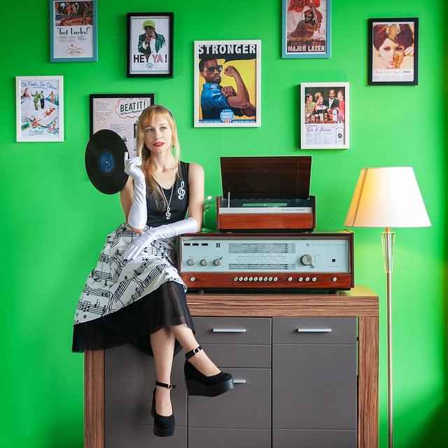 Women sat next to a large record player against a background of rock and roll pictures